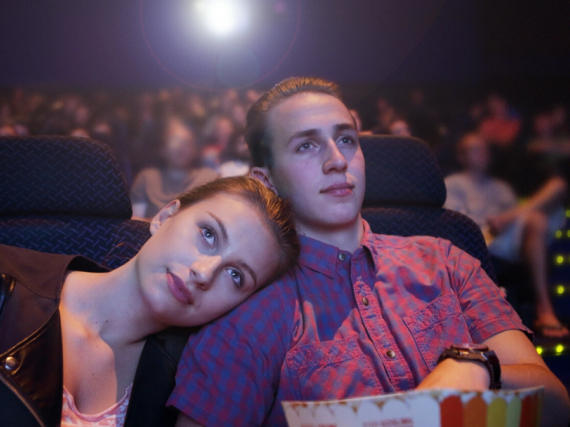 Two teens snuggle while watching a movie at the theatre. 