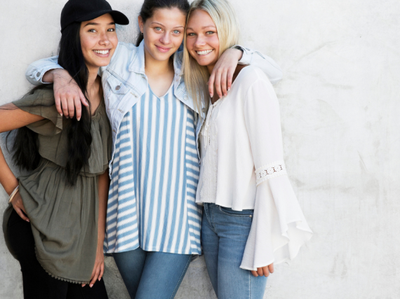 Three young women pose for a picture with their arms around each other and big smiles. 