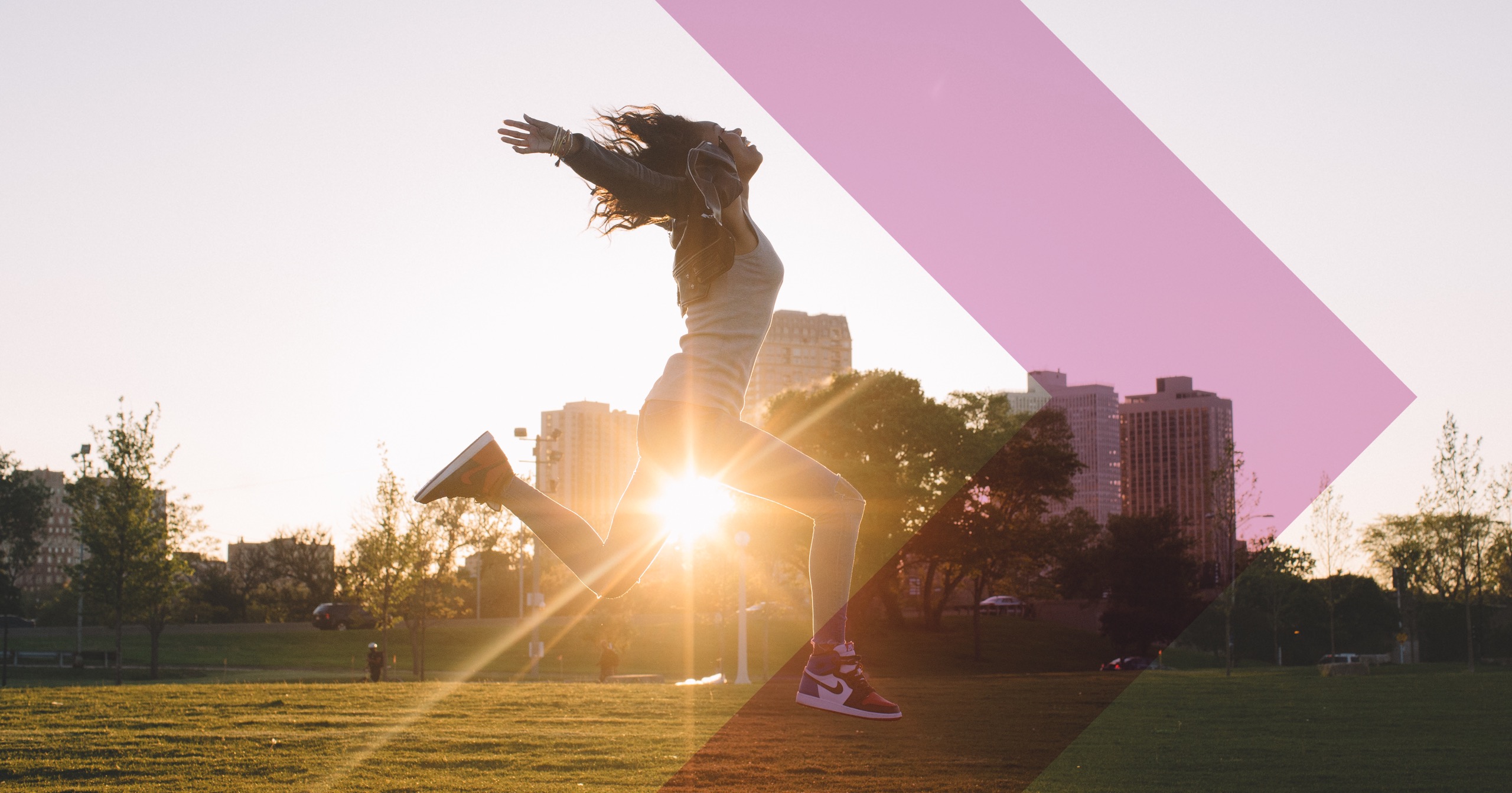 A woman jumps for joy in a field with the sun behind her