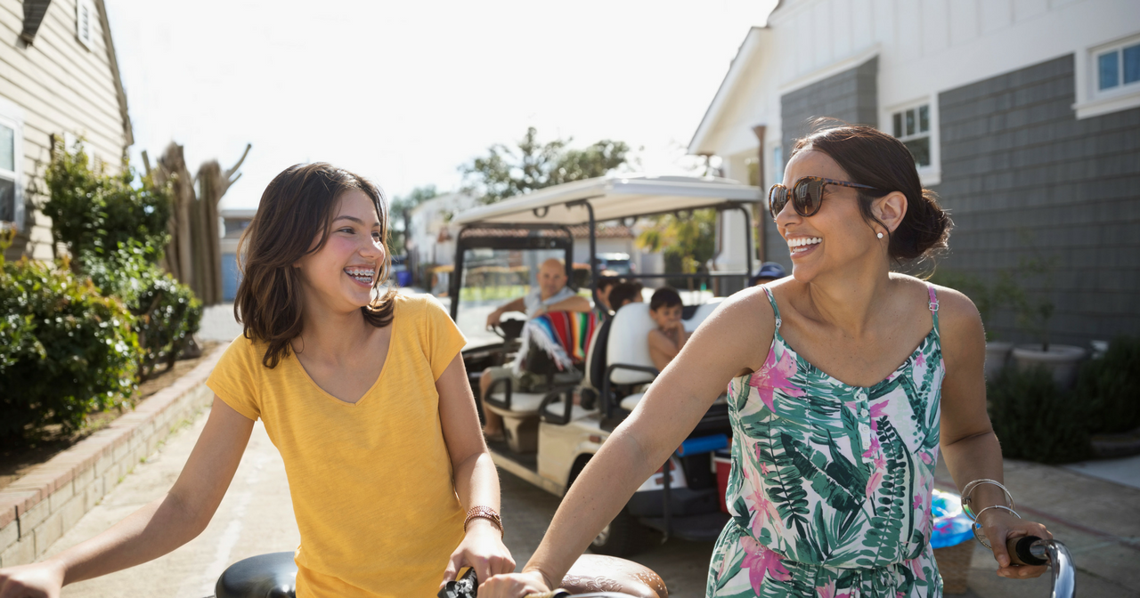A Latina mother and daughter walk their bikes along a street