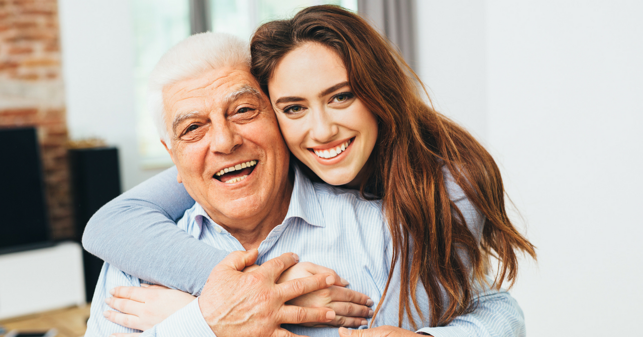 A daughter hugs her father from behind. 