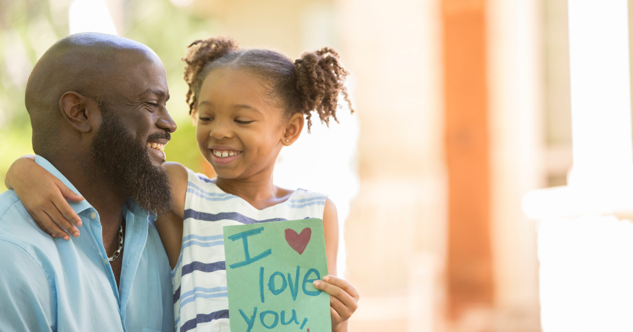 a young girl sits on her father's lap with a card that says, "I love you, dad."