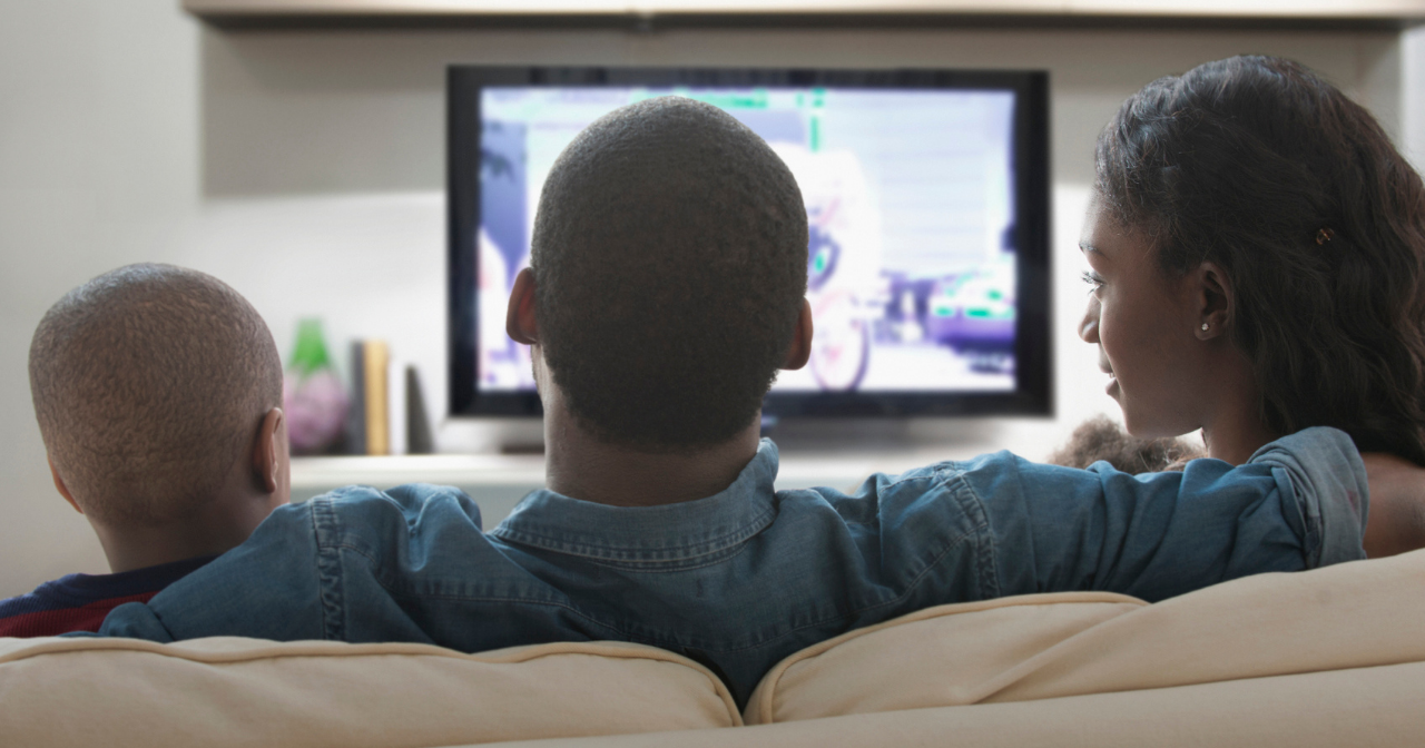 A family of three sits on the sofa and watches TV together 