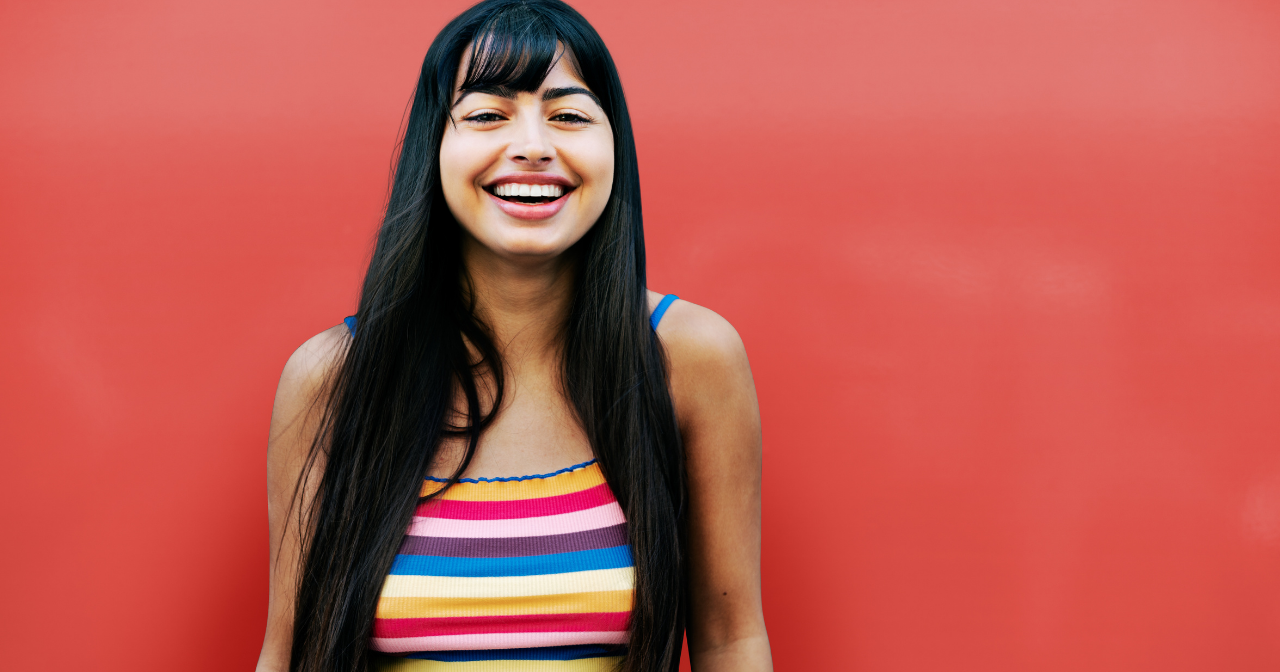 A woman smiling and laughing against a red background. 