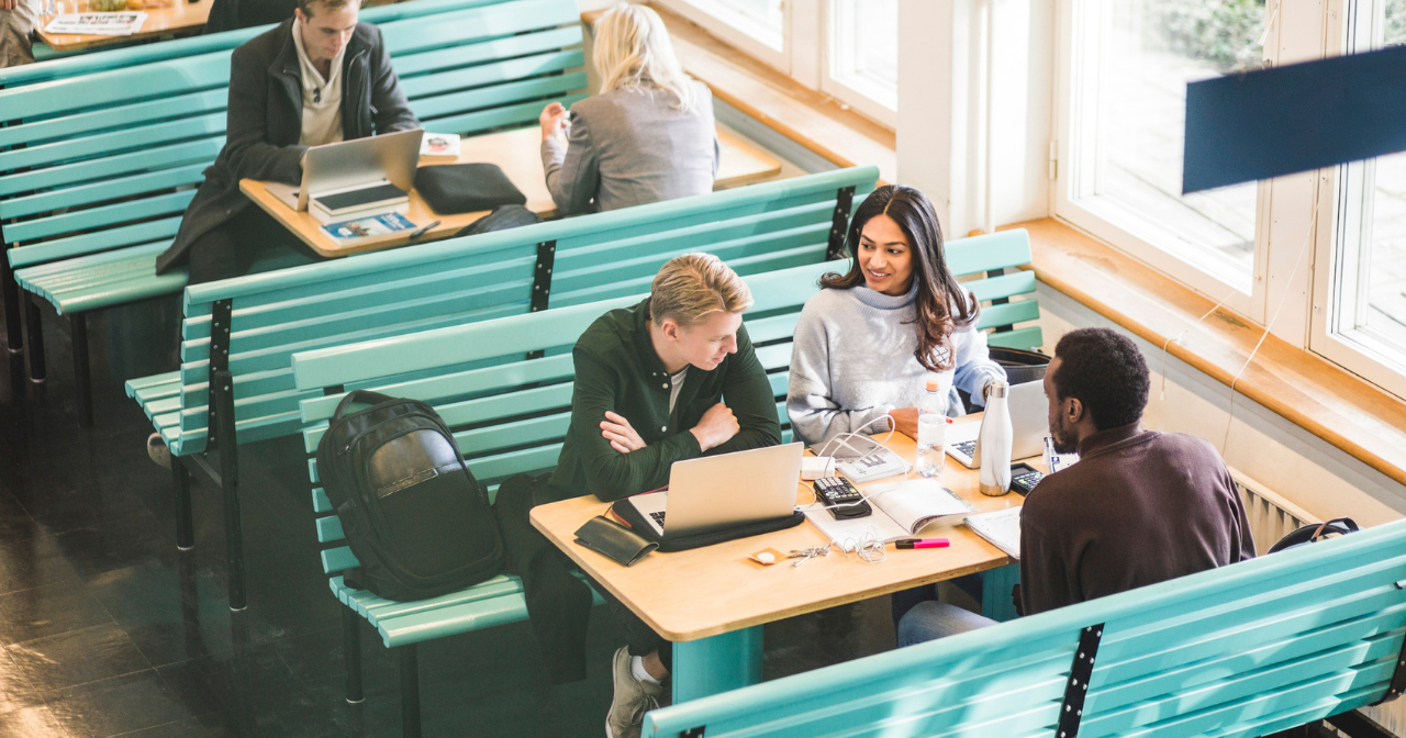 Three college students sit at a table together and do schoolwork. 