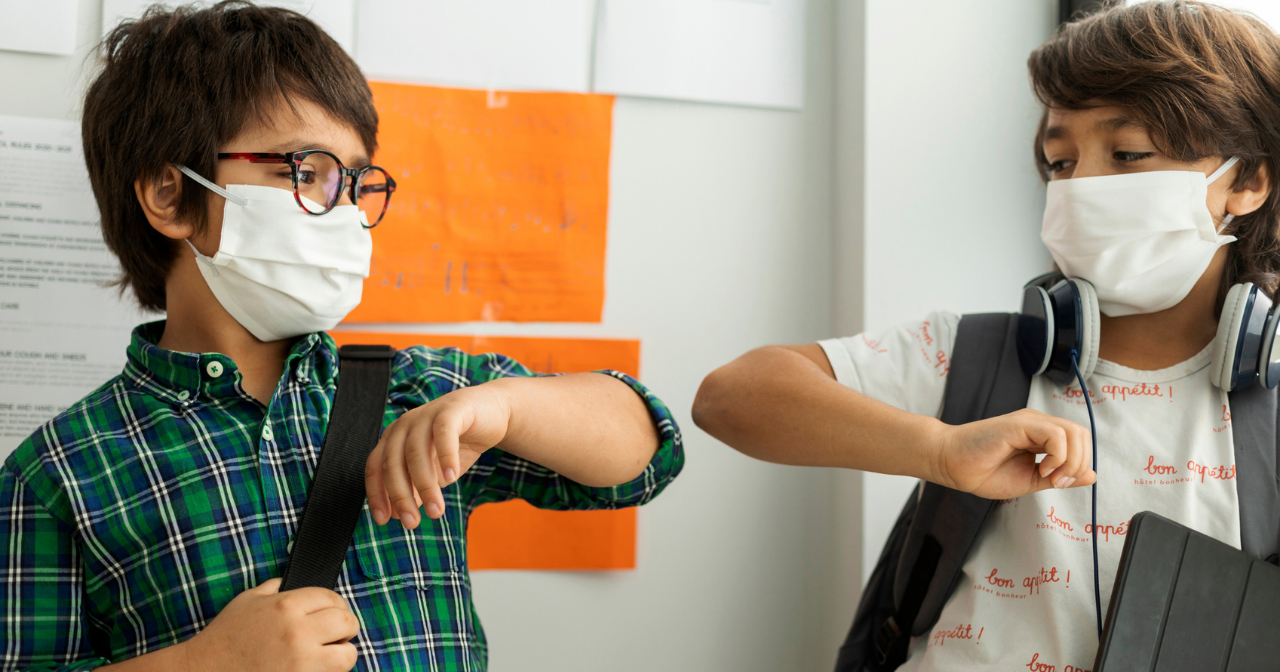 Two primary school age boys bump elbows while wearing masks to say hello in school. 