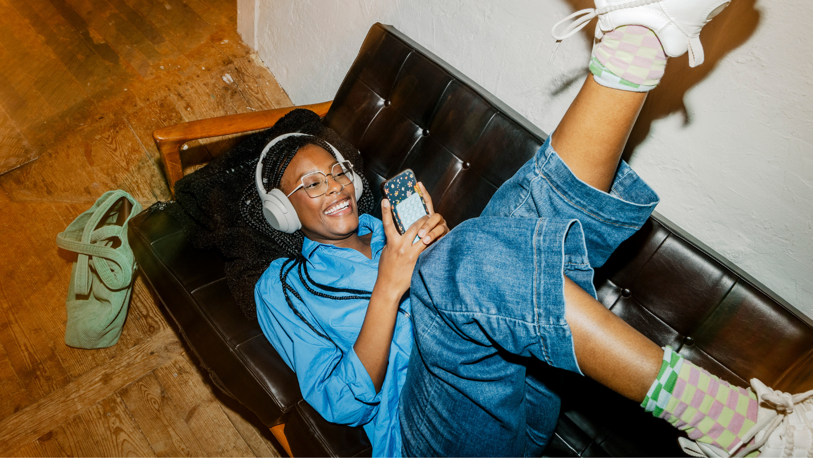 Person looking at phone and smiling with their feet up and on the couch.