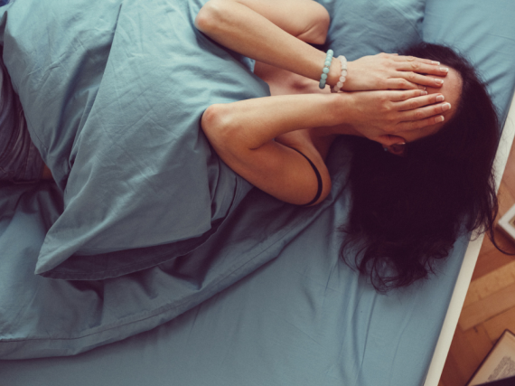 A woman holds her hands over her face in pain while laying in bed