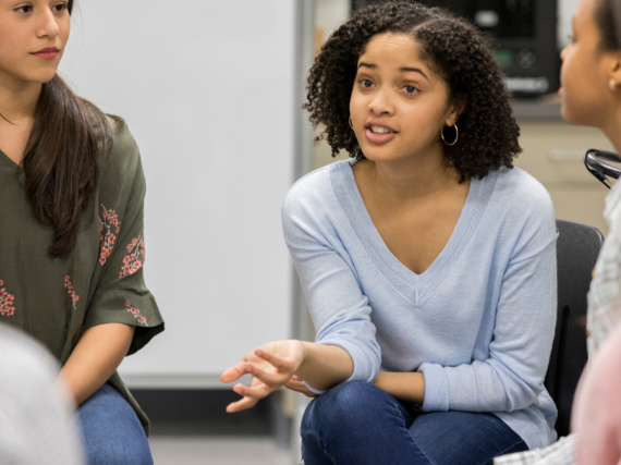 A group of teen girls sit in a circle and talk. 