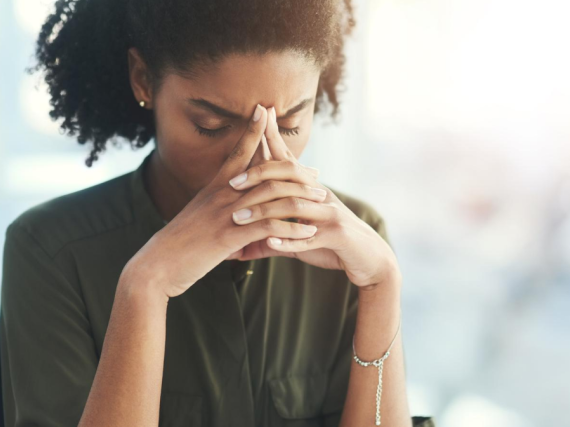 A Black woman sits with her hands over part of her face looking stressed. 
