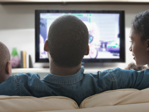 A family of three sits on the sofa and watches TV together 