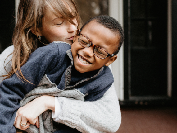 A mother and her son hug and laugh while sitting on their front step. 