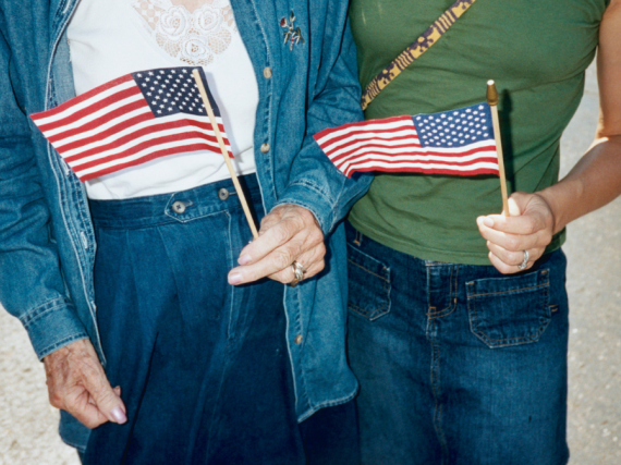 A photo of the torsos of two women standing on the street holding American flags. 