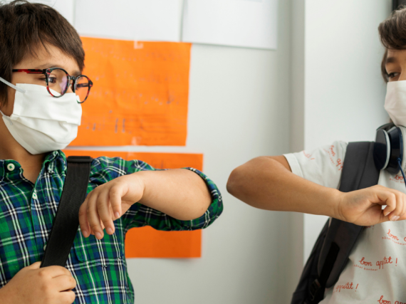 Two primary school age boys bump elbows while wearing masks to say hello in school. 