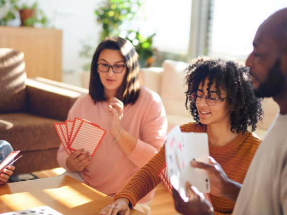 A family of four sits around their coffee table and plays a card game with oversized cards. 