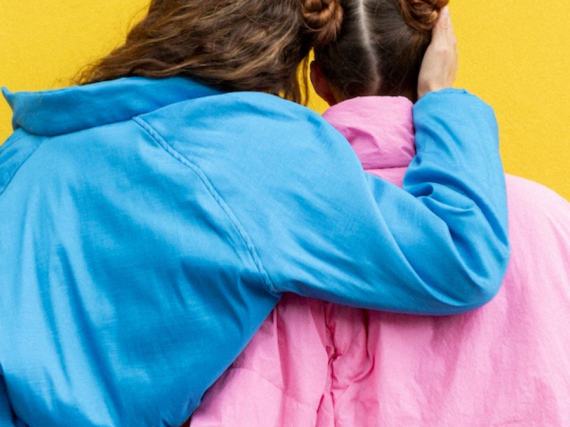 A photo of the back of two women in love who are hugging one another. 