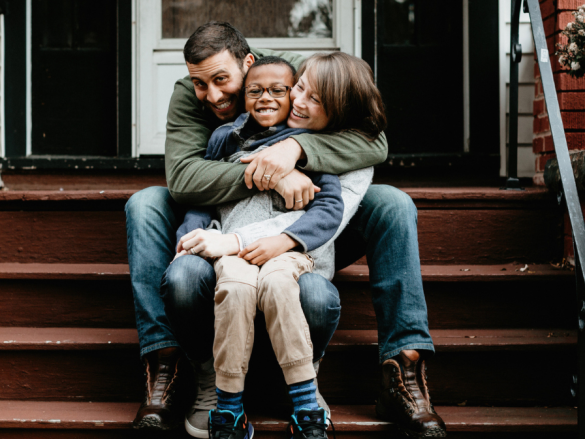 A happy family laughs and smiles sitting on the front stairs of their house.