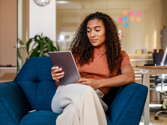A woman sits in a chair and reads on a tablet.